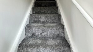Eine Treppe mit einem strukturierten Teppich, weißen Wänden und gerahmten Kunstwerken auf der oberen Landung.