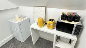 Eine kompakte Küchenzeile mit einem weißen Kühlschrank, einer Mikrowelle, einem Toaster und einer Kaffeemaschine auf einer weißen Arbeitsplatte.