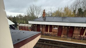 Ein Bahnsteig mit überdachtem Wartebereich und einem Backsteingebäude im Hintergrund.