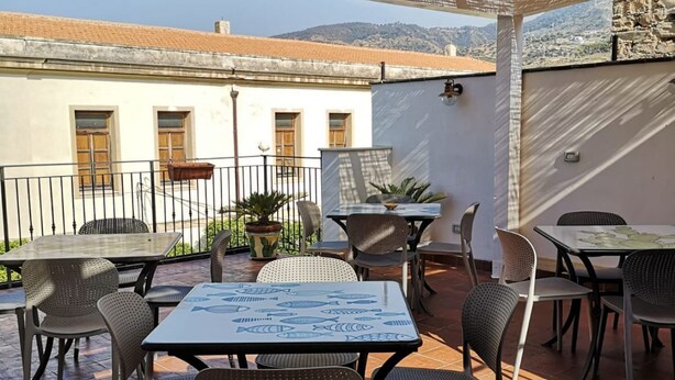 An outdoor patio with tables and chairs, a potted plant, and a view of a building with a tiled roof. - Salvia is an independent loft located on the ground floor, featuring a small private courtyard furnished with chairs and a table. The space consists of an open-plan area with a sofa bed and equipped kitchen, as well as a spacious bathroom with a shower.  (Santo Stefano di Camastra)