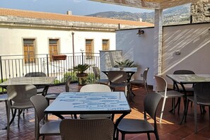 Un patio al aire libre con mesas y sillas, una planta en maceta y vistas de un edificio con tejado de baldosas.