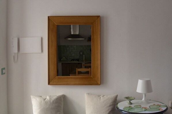 A room with a wooden-framed mirror, a small round table with a lamp, and two pillows.