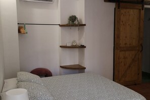 Un dormitorio con una cama, una silla roja y estanterías de madera con un reloj y una planta.