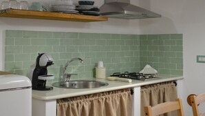 A compact kitchen with a sink, stove, and a coffee maker. - Salvia is an independent loft located on the ground floor, featuring a small private courtyard furnished with chairs and a table. The space consists of an open-plan area with a sofa bed and equipped kitchen, as well as a spacious bathroom with a shower.  (Santo Stefano di Camastra)