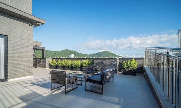 Une terrasse sur le toit, aménagée avec du mobilier d’extérieur, offrant une vue sur des collines verdoyantes et un ciel dégagé.