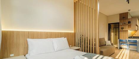 A hotel room with a bed, a desk, a chair, and a kitchenette.