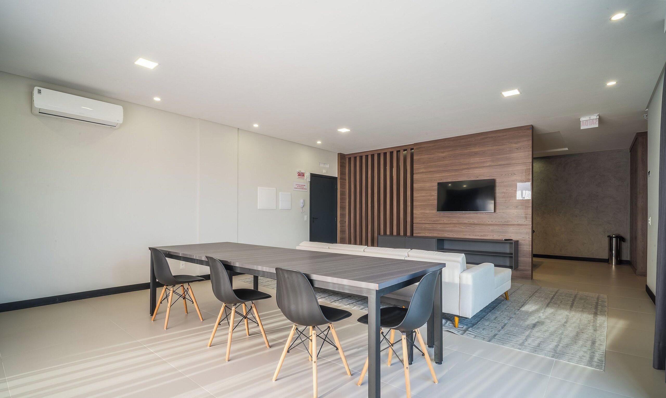 A modern office space with a long table, chairs, a sofa, and a mounted TV.