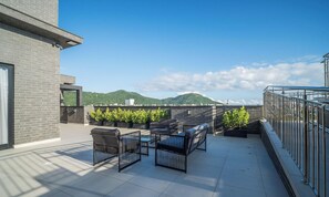 Una terraza en la azotea con mobiliario exterior, vistas a colinas verdes y cielo despejado.