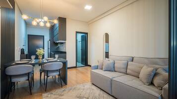 A modern living room with a sofa, a dining table with chairs, a chandelier, and a mirror.