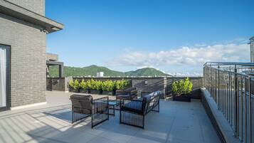 A rooftop terrace with outdoor furniture, a view of a mountain, and a building with a brick facade.