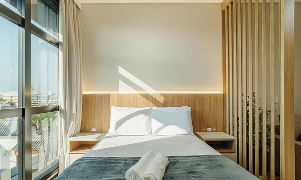 Een moderne hotelkamer met een groot bed, uitzicht door het raam en een houten scheidingswand.