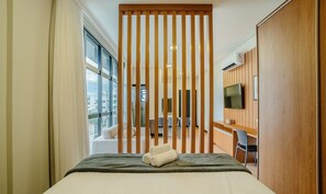 A hotel room with a bed, a TV mounted on the wall, and a view of the outside. - Complete Stay Just 550 Meters From Praia dos Ingleses - Ldus (Florianópolis)