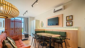 Une chambre d’hôtel moderne avec un coin repas, un canapé, une télévision et des œuvres d’art accrochées au mur.