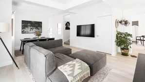 Ett modernt vardagsrum med en grå hörnsoffa, en platt-TV och en matplats med ett svart bord och stolar.