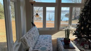 Una sala de estar acogedora con un sofá estampado, un árbol de Navidad y vistas a un lago a través de grandes ventanales.