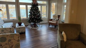 Un accogliente soggiorno con un albero di Natale, pavimento in legno e ampie finestre che offrono vista all'esterno.