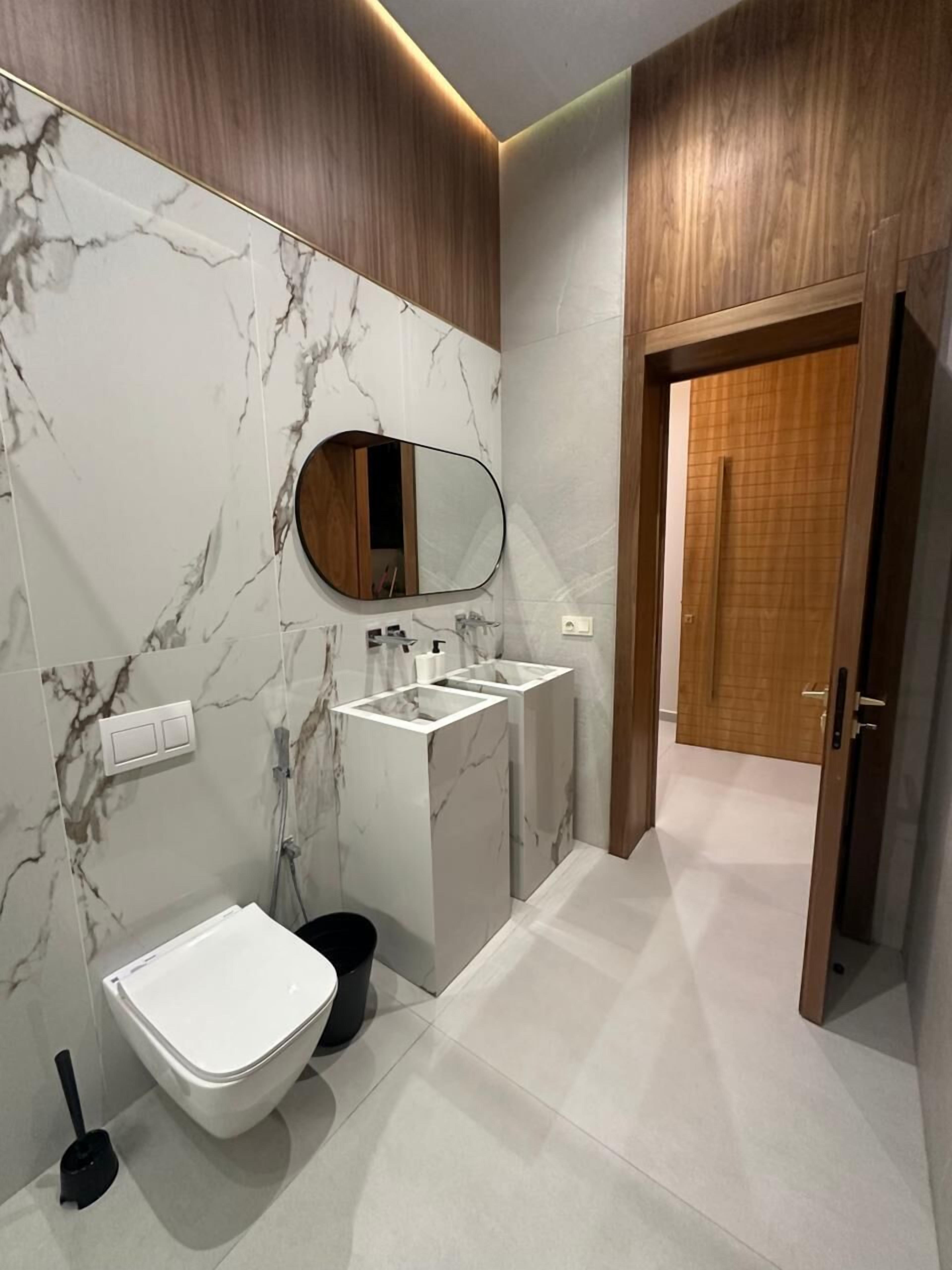 Een moderne badkamer met een marmeren wand, een vrijstaand badkamermeubel, een toilet en een houten deur.