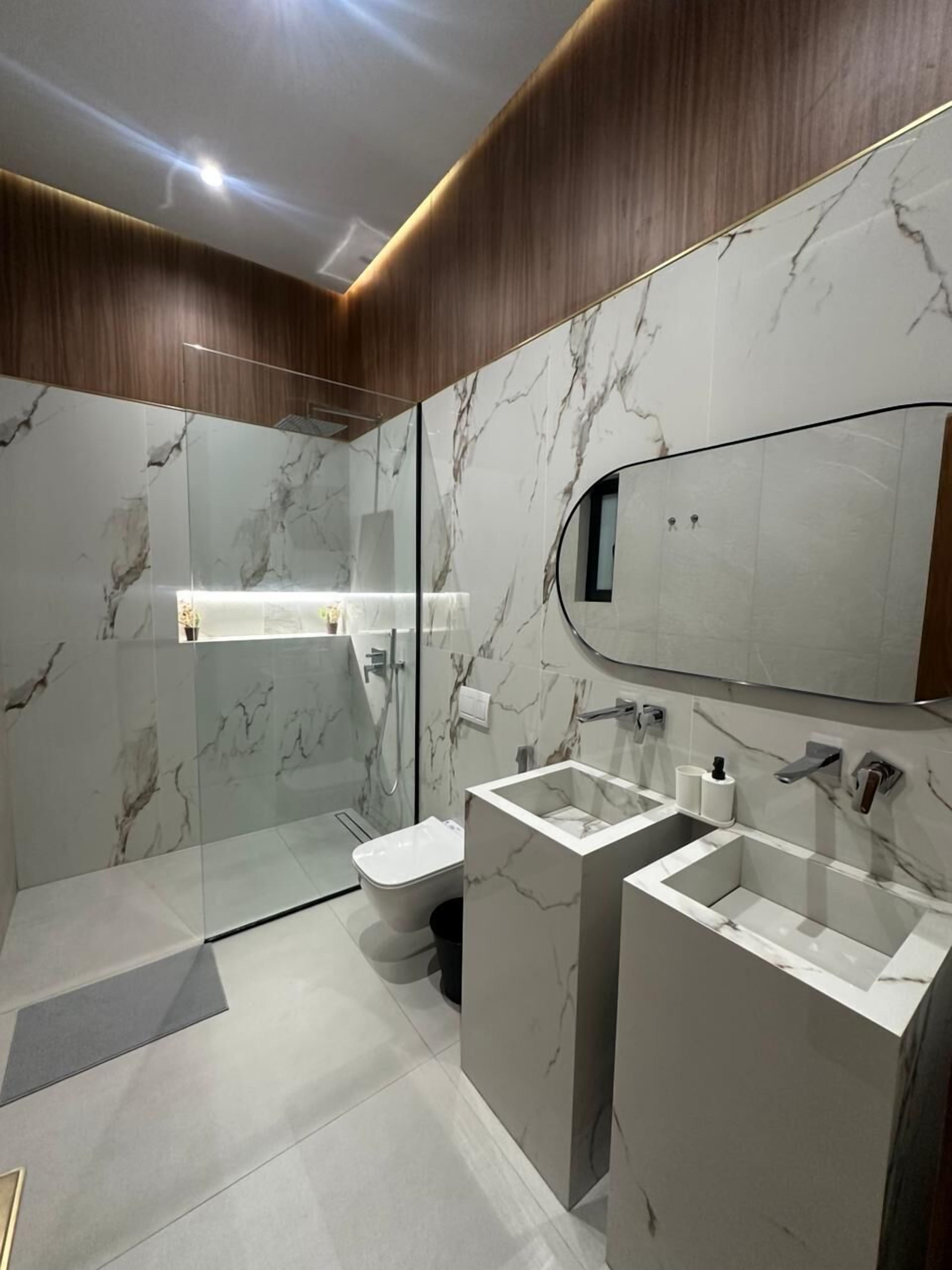 A modern bathroom with marble walls, a glass shower enclosure, and a large mirror.