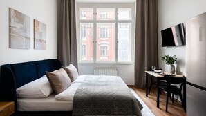 Une chambre à coucher avec un lit, un bureau, une chaise, une télévision et une fenêtre avec des rideaux.