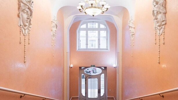 Un magnifique escalier recouvert d’une moquette rouge mène à une porte ornée d’un panneau de verre décoratif.