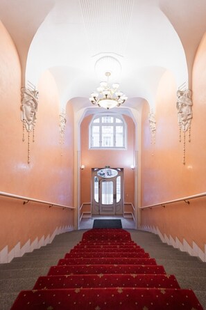 A grand staircase with red carpet leading to a door with a decorative glass panel. - Stylish Riverside Studio | City Center, Park & Smart TV by EasyBNB Premium (Prague)