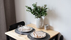 Une table à manger avec deux assiettes de nourriture, deux verres à vin, un vase contenant des feuilles vertes et une bougie.