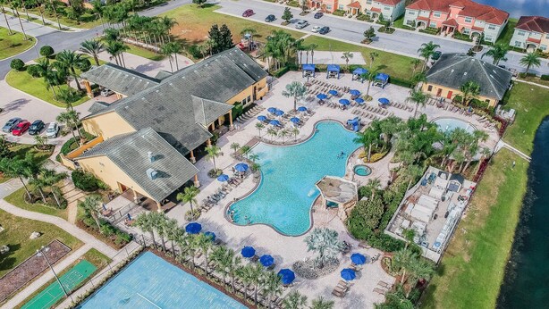 Luchtbeeld van een resort met een groot zwembad, ligbedden en een tennisbaan.