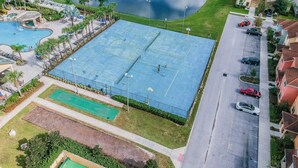 Luchtbeeld van een woongebied met een groot blauw tennisveld, een zwembad en een vijver.