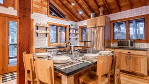 A wooden cabin kitchen with a dining table set for four, equipped with a stove, sink, and refrigerator. - West Shore Home with Private Hot Tub (Tahoe City)