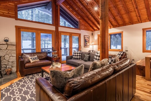 Ein gemütliches Wohnzimmer mit Kamin aus Stein, Ledersofas und großen Fenstern mit Blick auf die verschneite Landschaft.