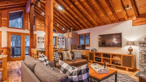 A cozy living room with a wooden ceiling, a leather sofa, a television, and a stone fireplace. - West Shore Home with Private Hot Tub (Tahoe City)