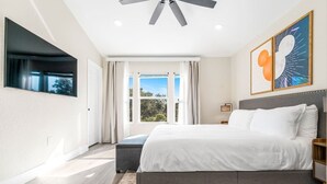 Una camera da letto moderna con un letto grande, un ventilatore a soffitto, una TV a parete e una finestra con tende.