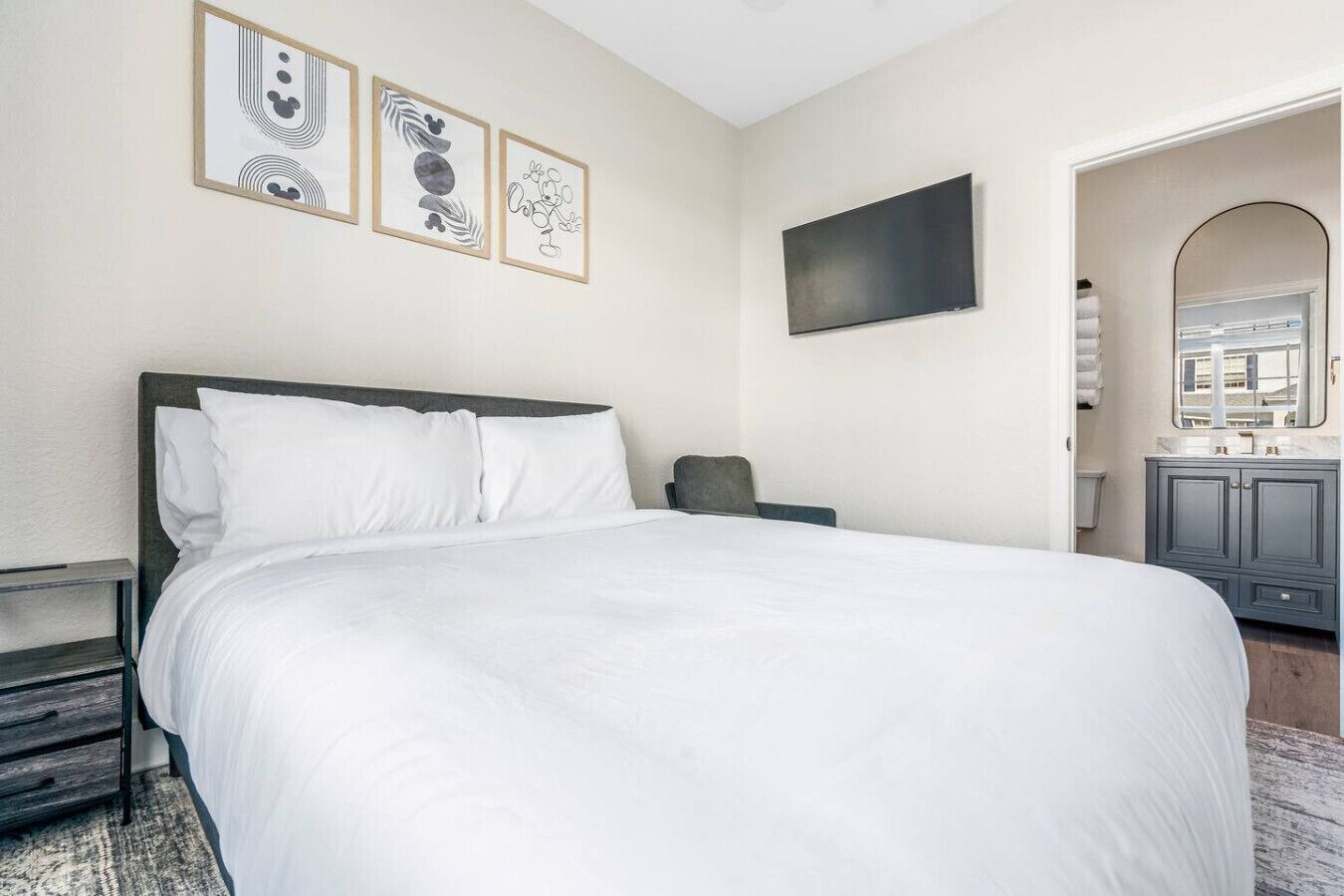 A neatly made bed with white linens in a room with a gray headboard. There are three framed artworks on the wall above the bed.