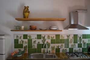 Cozinha com painel de azulejos verde e branco, pia de aço inoxidável e fogão a gás.