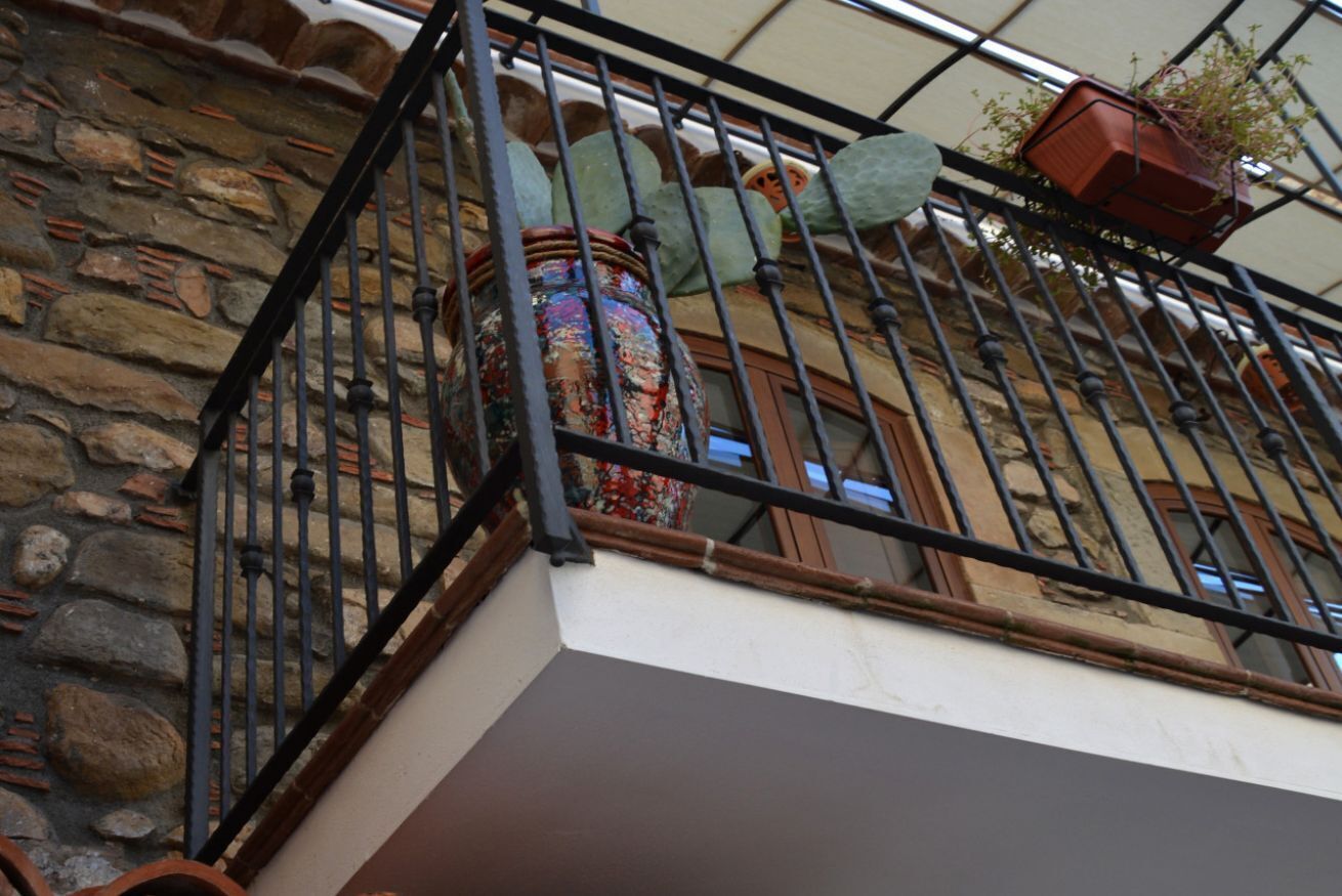 A stone building with a metal balcony railing, a large decorative vase, and a potted plant.