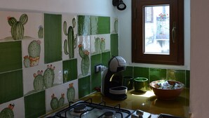 Eine Küche mit grün-weißen Fliesen, die Kaktusmuster zeigen, einem Kaffeeautomat, einer Schüssel und einem Fenster mit Blick ins Freie.
