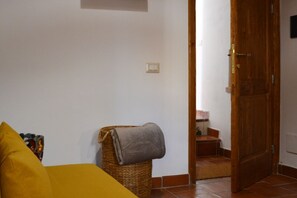 Een kamer met een bed, een rieten mand met een deken, een houten deur en een kleine trap naar een badkamer.