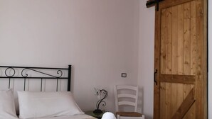 Ein Schlafzimmer mit einem Bett, einer Holztür, einem weißen Stuhl und einem kleinen Tisch mit einem dekorativen Gegenstand.