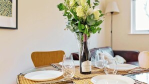 A dining table set with plates, glasses, and a wine bottle, surrounded by chairs and a decorative vase with flowers. - 2BR Docks View Flat With Free Parking Terrace Fast WiFi TV BBQ PrivateGarden (London)