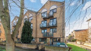 A multi-story building with balconies, a large tree in front, and a paved walkway. - 2BR Docks View Flat With Free Parking Terrace Fast WiFi TV BBQ PrivateGarden (London)