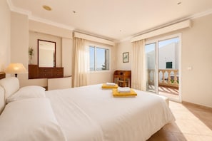 Quarto de hotel com uma cama grande, uma escrivaninha, uma cadeira, um espelho e uma varanda com vista.