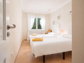 A bedroom with two beds, a window with curtains, a bedside table with a lamp, and a door with a handle. - Villa Casa Faro - Four Bedroom Villa, Sleeps 8 (Mallorca)