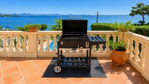 Ein tragbarer Grill auf einem Balkon mit Blick auf das Meer und die Berge.