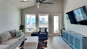 A modern living room with a sofa, ottoman, and a television on a cabinet. - Serenity at Port A (Port Aransas)