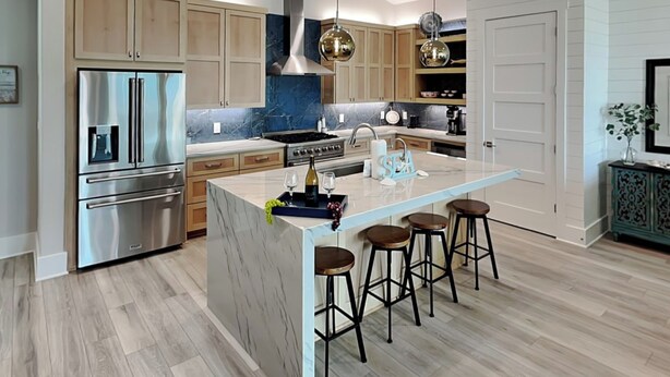 A modern kitchen with stainless steel appliances, a marble island, and bar stools. - Serenity at Port A (Port Aransas)