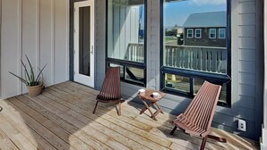 A balcony with wooden flooring, two wooden chairs, a small table, and a potted plant. - Serenity at Port A (Port Aransas)