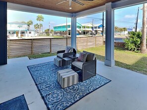 A covered patio with outdoor furniture, a patterned rug, and a view of neighboring houses. - Serenity at Port A (Port Aransas)