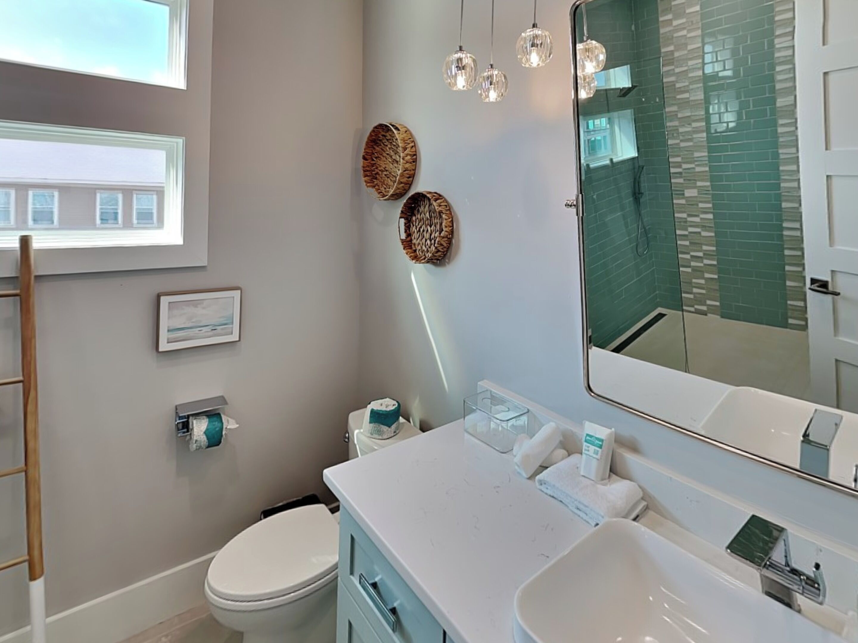 A modern bathroom with a toilet, sink, and mirror. There are decorative baskets on the wall and a window above the toilet.