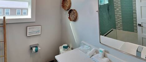 A modern bathroom with a toilet, sink, and mirror. There are decorative baskets on the wall and a window above the toilet.