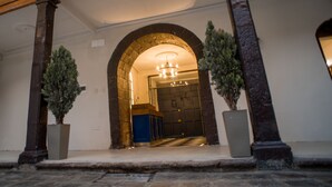 Una entrada arqueada con una araña, columnas de piedra y plantas en macetas.